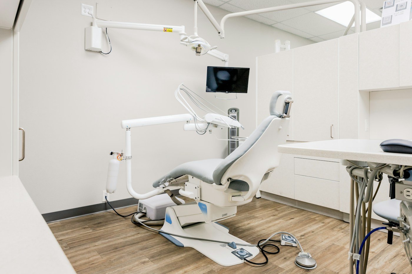 Modern dental treatment room with a gray dental chair and white cabinetry